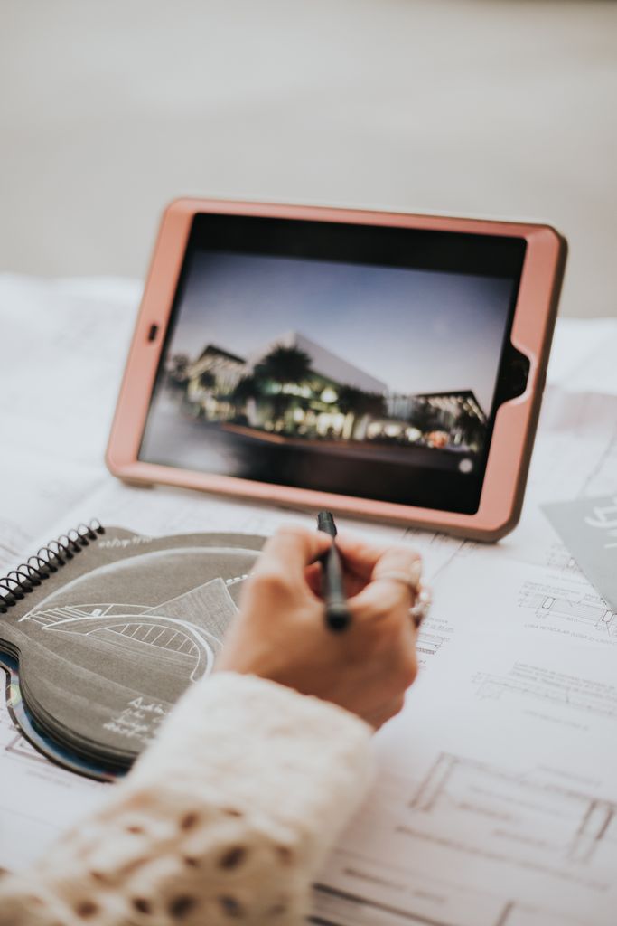 Architect drawing on a tablet with building plans, showcasing design creativity and technology.