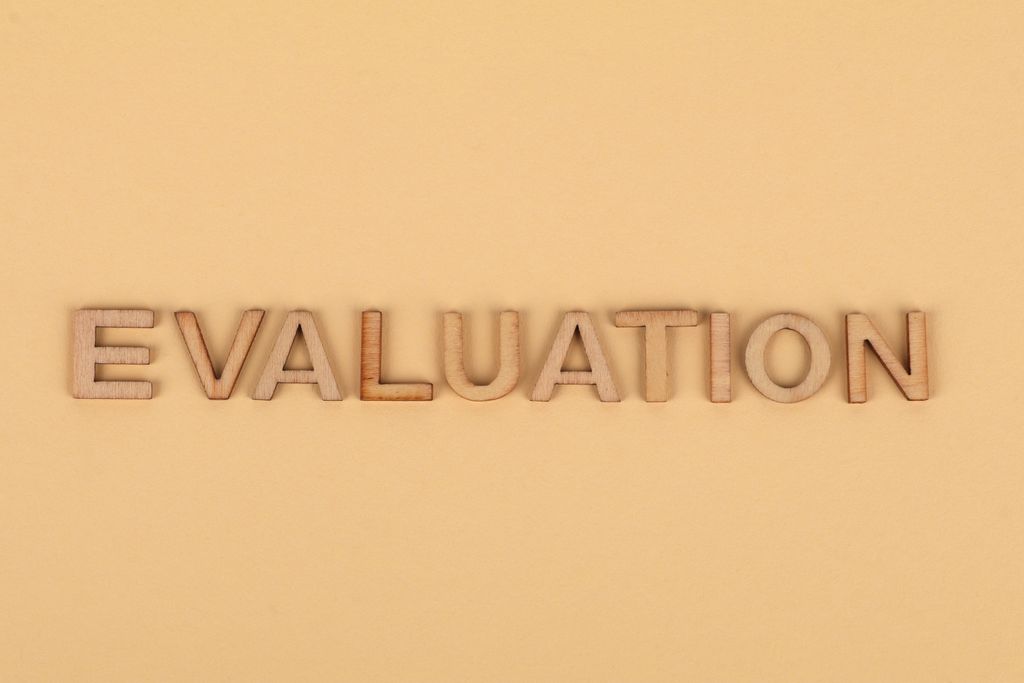 Wooden letter blocks arranged to spell 'evaluation' on a beige background.