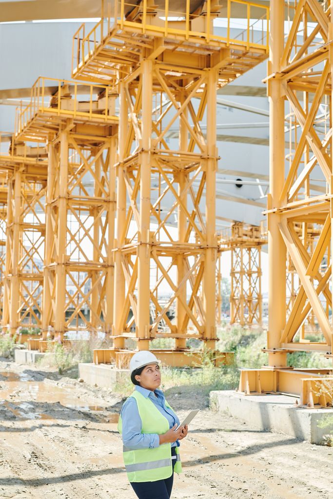 A professional woman engineer in safety gear examines the large construction framework outdoors.