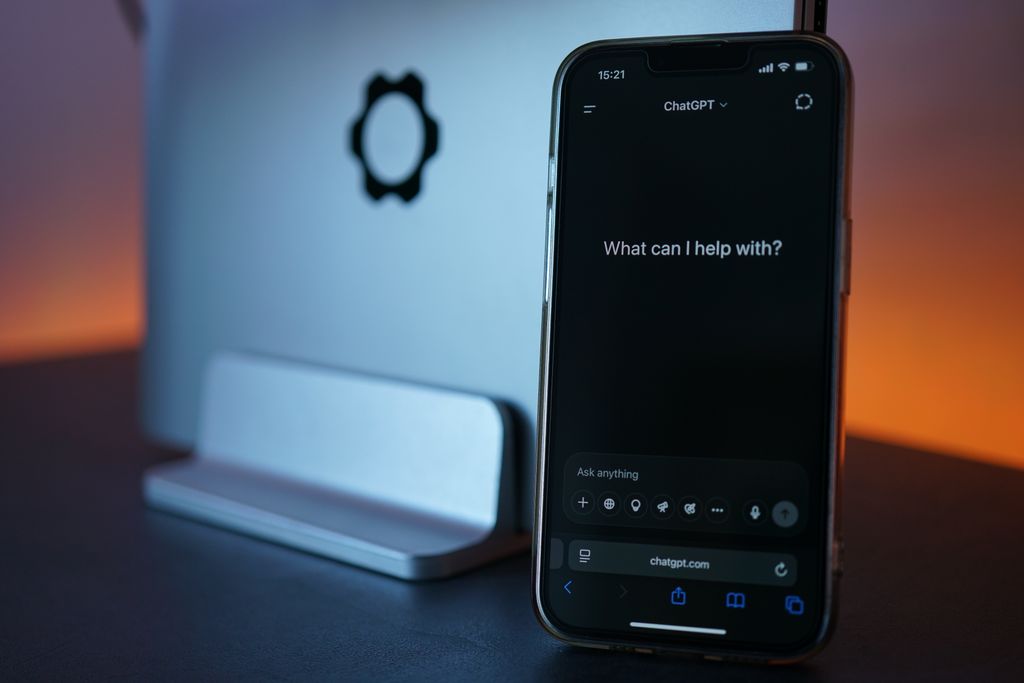 Close-up of a smartphone showing a chat interface with a laptop in the background.