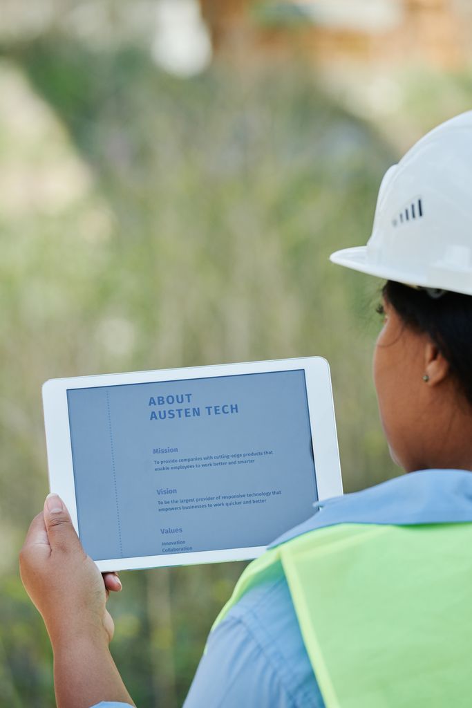 A construction worker examines site plans on a digital tablet outdoors.