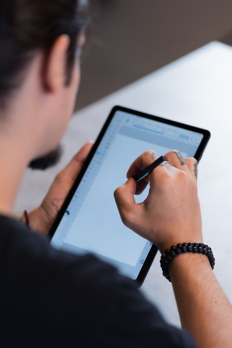 Close-up of a man drawing on a tablet with a stylus indoors, focusing on hand movement.