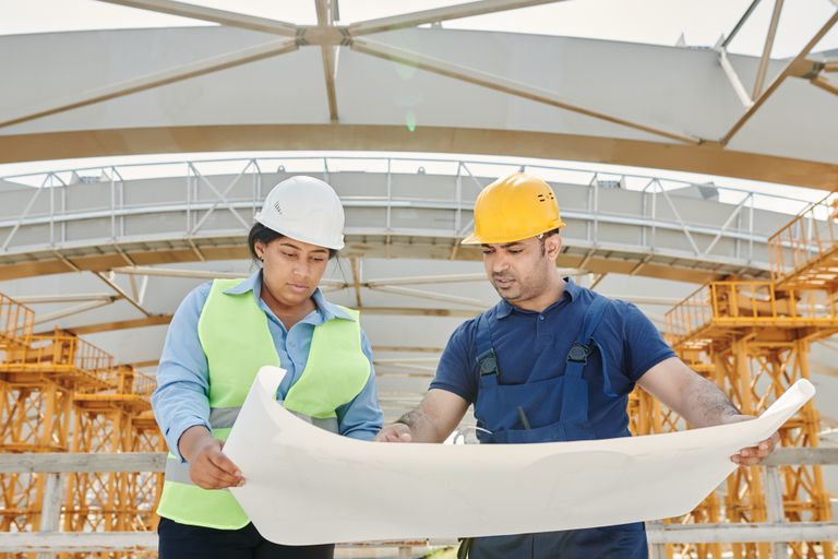 Male and female engineers discussing blueprints at a construction site, promoting teamwork and planning.