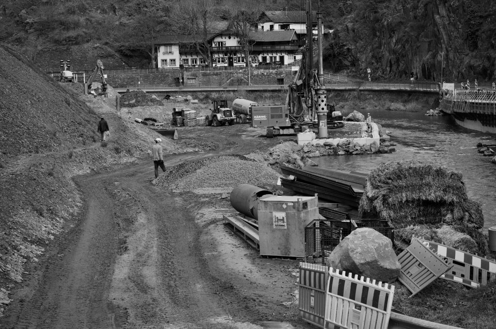 Monochrome image of construction site next to a river with heavy machinery and workers.