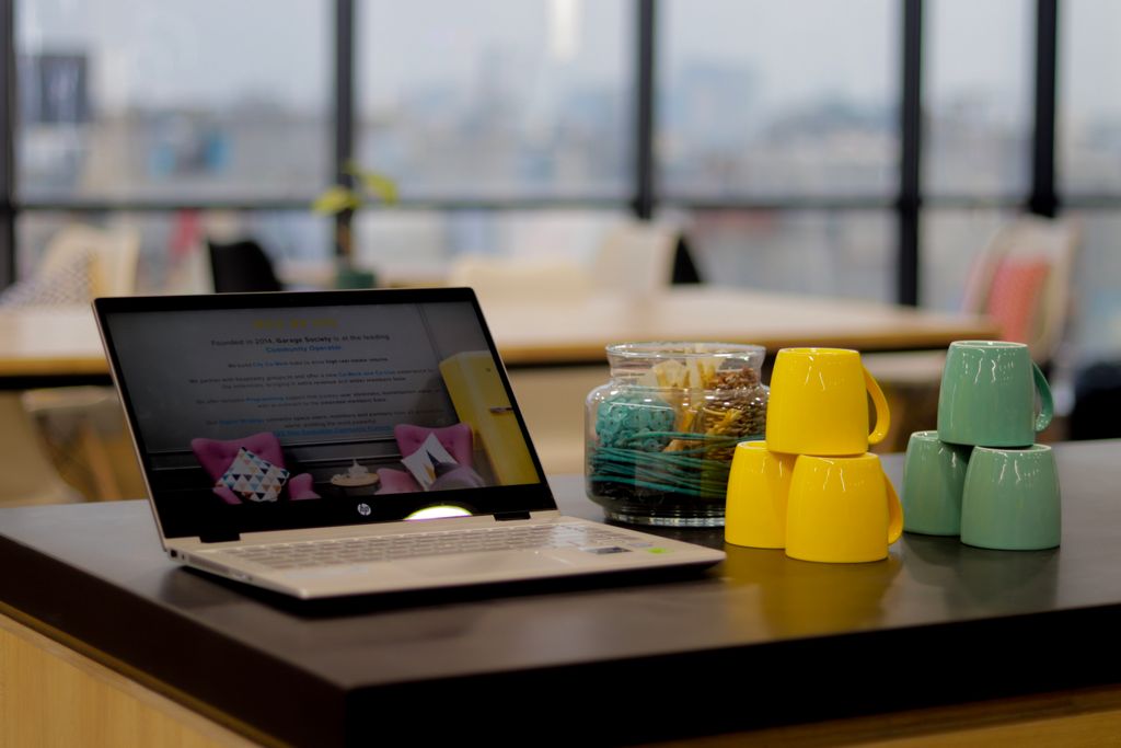 Sleek laptop on a desk with colorful stacked mugs in a bright office setting.