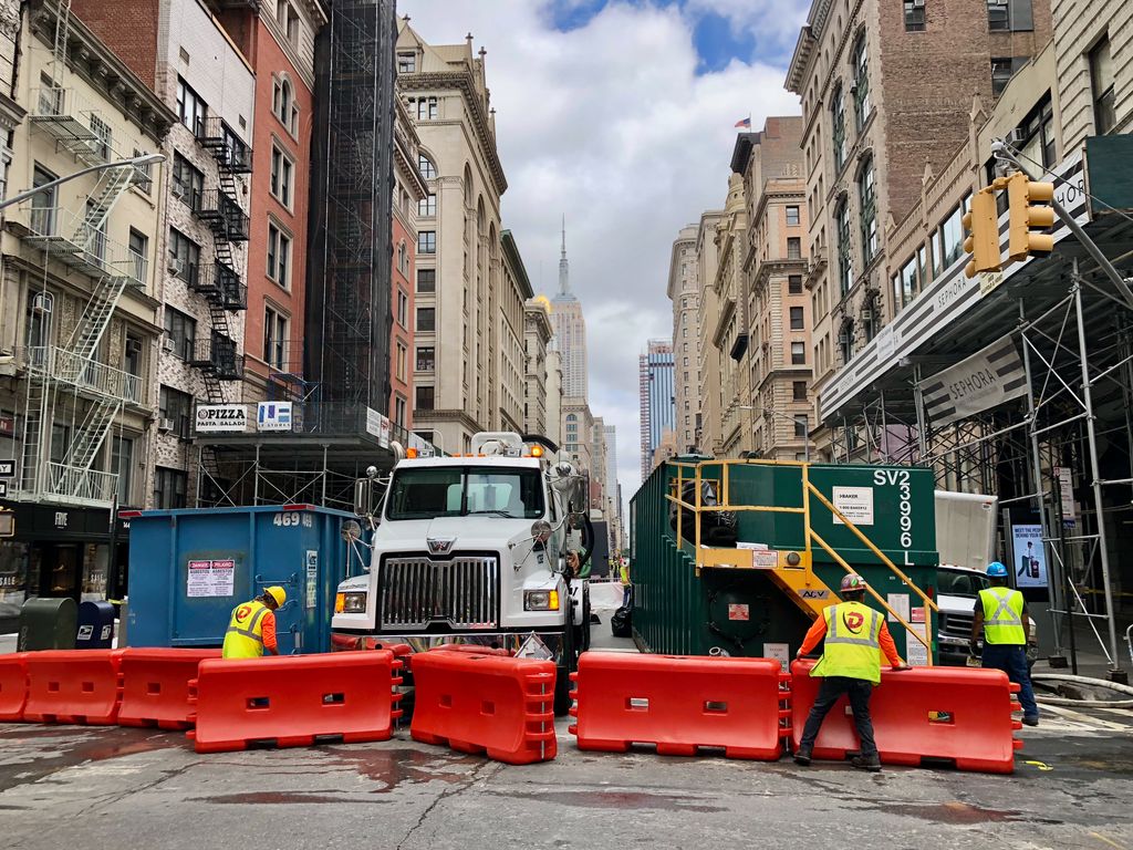 Urban construction site in New York City street with visible Empire State Building.